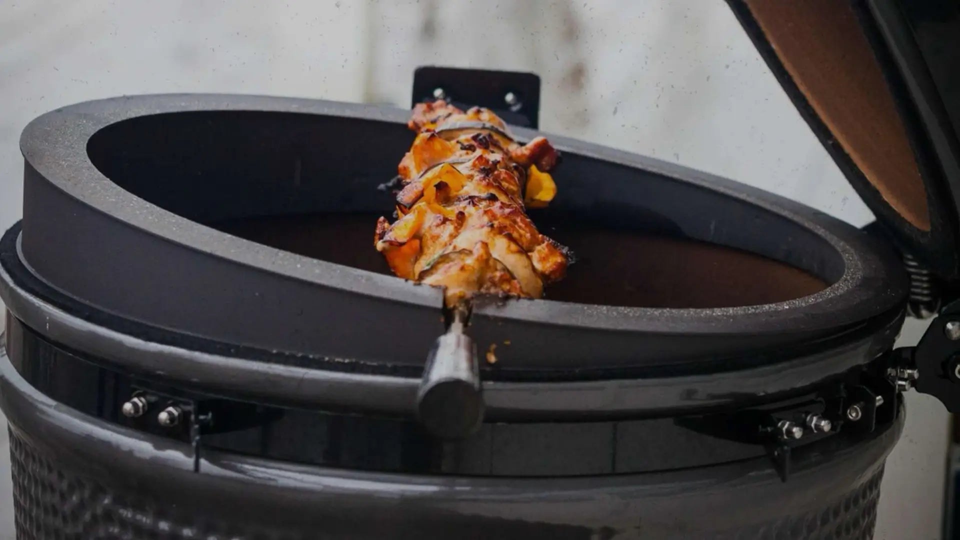 Nahaufnahme eines Kamado-Grills mit rotierenden Hähnchenspießen auf dem ‚Spit on Fire‘-Rotisserieaufsatz, exklusiv bei miori.
